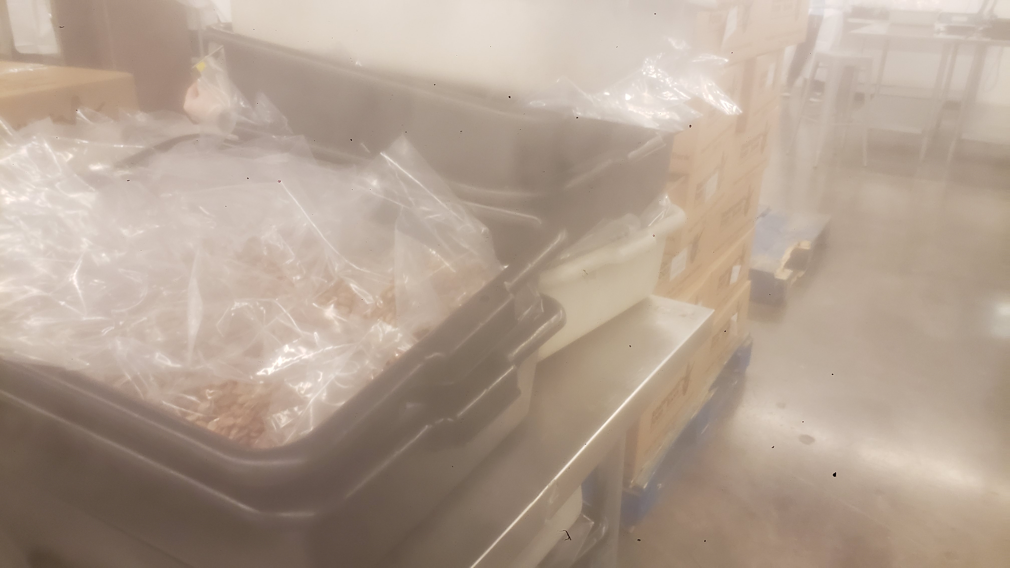 Pile of tubs with the top two filled with bagged pinto beans and a row of boxes on a pallet next to it.